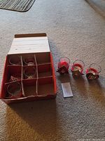 Set of 6 glass candle holders in a cardboard box on carpeted floor, 3 holders shown outside of box.