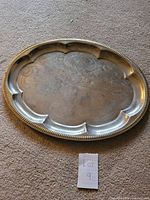 Large oval silver serving tray with ornate scalloped edges and detailed floral etching, some tarnish visible