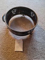 Photo showing tarnished round silver trivet on carpet, one handle visible, missing the opposite handle, with decorative cut outs.