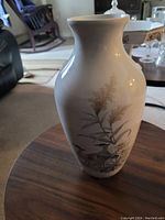 Side view of the large white ceramic vase with botanical design on wooden table.