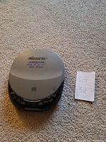 Top view of Memorex portable CD player in closed position on carpeted floor next to a piece of paper with Lot 32 written on it.