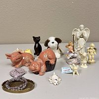 Collection of porcelain animal and angel figurines, including pigs, cat, dog, and cherubs, displayed on a flat surface.