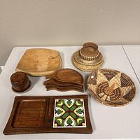 Photo of various wood decorative items including cheese plate, leaf trays, wooden container, and circular woven basket.