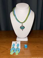 Full view of necklace on display bust, displayed with earrings on card and ring on table