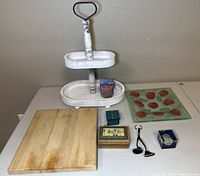 Overview of all items on a table showing the two-tiered display caddy, wooden cutting board, glass serving tray with fruit motifs, decorative boxes, and keychain items.