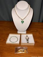 Wide shot of all jewelry items on display, showing the pearl necklace on a bust, the Anne Klein watch in a box, a green beaded bracelet in a box, and a small plastic bag containing a gold-tone beaded bracelet.