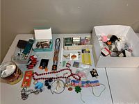 Overview of the entire lot spread on a table showing a wide collection of costume jewelry items, pins, beads, ribbons and packaged sewing supplies.