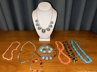 Front view of the collection of costume jewelry including necklaces displayed on table and mannequin bust.