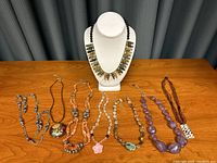 Eight assorted costume jewelry necklaces displayed on table and bust showing variety of beads and pendants.