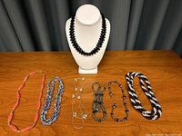Group of seven assorted beaded necklaces displayed on a wooden surface with neutral background.
