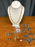 Full group of costume jewelry items including necklaces, earrings, rings, a brooch, and a cactus pendant displayed on wooden surface with white necklace stand.