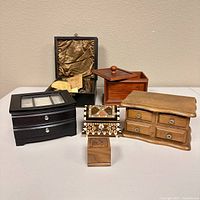 Six wooden jewelry boxes arranged on a white surface against a beige wall, showing various designs and sizes.