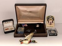 Group of souvenir pins, Mickey Mouse pin with backing card, American flag pin, duck pins, some housed in boxes, and mallard duck figurine in front.