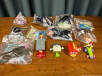 Grouping of multiple McDonald's Happy Meal toys, some in original plastic packaging, arranged on a wooden surface.