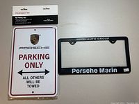 Photo of sealed Porsche Parking Only sign packaging and black Porsche Marin license plate cover frame.