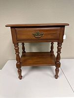 Full view of medium brown wooden side table with single drawer, turned legs, and bottom shelf. Shows distress on top.