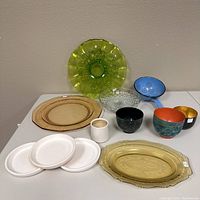 Full view of various serving items including glass plates, Asian cups, and enamel strainer