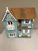 Front and side exterior view of the vintage teal Victorian dollhouse with detailed white trim and brown shingled roof, showing wear and distress.