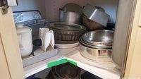 Corner interior shelf holding multiple metal baking pans, springform pans, pie plates, and Pyrex baking dish
