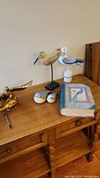 Photo of five bird ornaments arranged on a wooden dresser, including two mounted shorebird figurines, two small wooden birds, a brass bird sculpture, and a bird-themed trinket box shaped like a book.