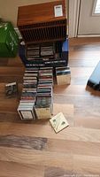 Photo of wooden CD storage case on top of a box with 150+ CDs arranged in rows on floor