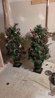 Photo of two 33-inch artificial Christmas trees with decorative greenery, berries, pinecones, set in heavy ceramic urn pots.