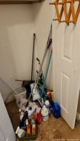 View of mop and broom handles alongside various bottles of cleaning liquids arranged on tiled floor.
