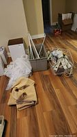 Overall view of the lot items on wood floor — curtain rods, sheers, wire baskets, power bars, timers, and underpadding.