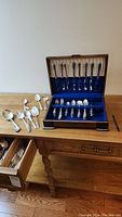Full view of the silver-plated flatware set arranged in and out of the wooden canteen with blue interior lining