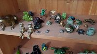 Shelf with an assortment of metal and ceramic frog figurines, various sizes and colors.