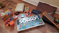 Overview of various board games, card decks, dice and game pieces scattered on floor including Sorry game, Boggle boxed games, decks of cards and dice.