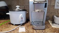 Photo of white Proctor Silex rice cooker RC09 beside silver Keurig coffee maker on a countertop.