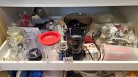 Overview of kitchen appliances and utensils including Magic Bullet, mixing bowls, cookie cutters, and other items inside a cabinet shelf