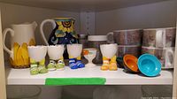 Shelf with pitchers, boot-shaped egg cups, white floral egg cup, and mugs