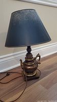 Full view of lamp showing teapot style base and dark blue shade with rip and wear.