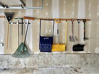 Photo of multiple garden tools hung on a wall for sale, including rakes, shovels, brooms, and weed removers.