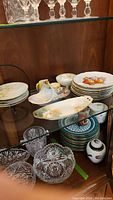 Photo of multiple plates, bowls, creamer, and sugar bowl arranged on shelves showing the variety of items.