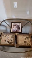 Three framed Asian themed prints on a glass table, including one print featuring a pavilion and boat and two prints featuring women with birds and foliage.