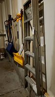 Side view of the aluminum ladder leaning against the wall with some tools hanging nearby.