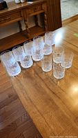 Photo showing two groups of crystal tumblers, one group of 9 and one group of 4, on a wooden table.
