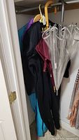 Closet photo showing two umbrellas and two pant suits hanging on hangers.