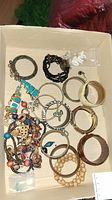 Photo showing assortment of bracelets and necklace with mixed materials and colors in a cardboard box.