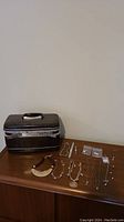 Photo showing multiple necklaces, earrings, watches, and a black Samsonite makeup case on a wooden surface, with a brown jewelry bag beside.