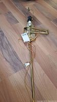 Brass wall lamp laying flat on wood floor with visible articulating arm, bulb socket, and power cord with plug.