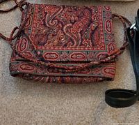 Red and brown paisley fabric purse with fabric strap lying on carpet.