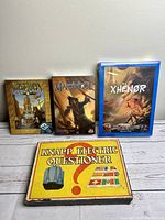 Front view of the four games showing three new sealed board games Scarab Lords, Martinique, Xhenor plus a vintage Knapp Electric Questioner board game in a yellow box.