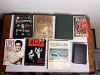 Seven books arranged on a table, showing titles and covers including David Copperfield's History of Magic, Ancient Egypt, William Shatner's TekLords, two Elvis Presley books, Currier & Ives Chronicles of America, and a green hardcover book.