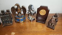 Photo showing 5 metal bookends lined up on a wooden table: an eagle with blue base, stylized horse head, bear pair, and a carved wooden plaque