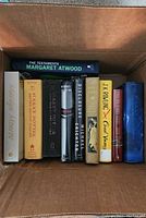 Top view of box with ten hardcover books including Marilyn Monroe, Harry Potter series, Michael Crichton, Margaret Atwood, Da Vinci Code, and J.K. Rowling titles
