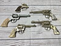 Top view of all five toy guns arranged on white wood grain background showing size variation and grip details
